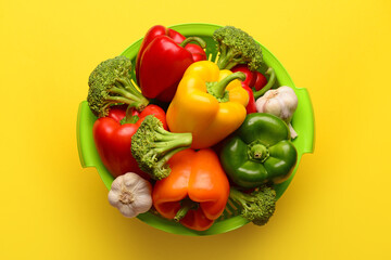 Colander with different fresh vegetables on yellow background