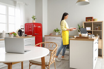 Young woman cooking sausages on electric grill in kitchen