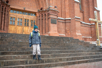 happy child goes to catholic church on sunday in winter. A 10-year-old boy stands in front of a...