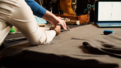 Student and old tailor cutting material for handcraft in atelier, beginner using scissors to cut fabric before sewing and designing clothes. Couturier and apprentice. Handheld shot. Close up.