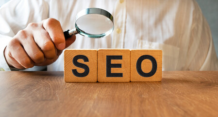 SEO inscription on the texture of wooden cubes. A business man holds a cube in his hand. An...