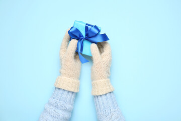 Female hands in warm mittens with Christmas gift on color background, closeup