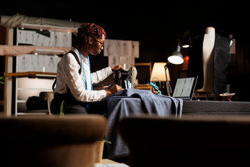 Seamstress looking for inspiration online, using industrial sewing machine to do creative embroidery on garments. Suitmaker working on upcoming handmade bespoken clothing in tailoring studio