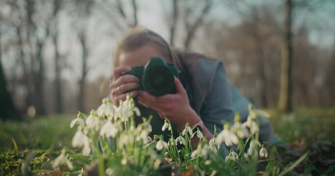 Woman photographing snowdrop flowers through camera