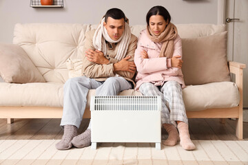 Frozen young couple warming near radiator at home