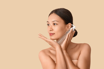 Young Asian woman with bottle of micellar water on beige background, closeup