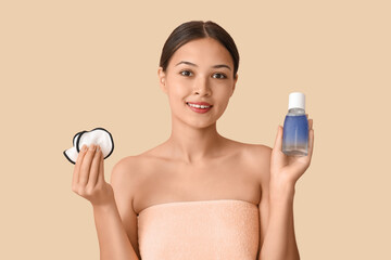 Young Asian woman with bottle of micellar water and reusable cotton pads on beige background