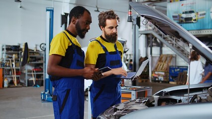 Mechanic listening to customer in auto repair shop, using tablet to write down car modifications she wants to make. Expert in garage with client, listening to her requests for vehicle tuning
