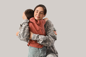 Female soldier hugging her little son on light background. Veterans Day celebration