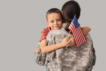 Little boy with USA flag hugging his military mother on light background. Veterans Day celebration