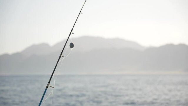 Close up of rod with fishing sinker on the fishing line ready to catch big fish in the sea. Mountains in the background at sunset
