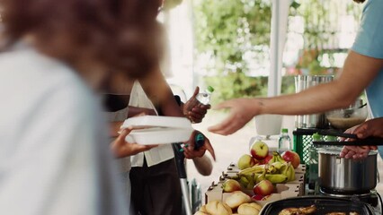 Voluntary individuals contributes to and offers humanitarian help to the underprivileged and needy. Young black volunteer woman helps african american guy using crutches at a food drive. Tripod shot.