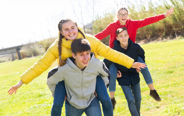 Happy teenage friends having fun together in spring city park, boys piggybacking girls