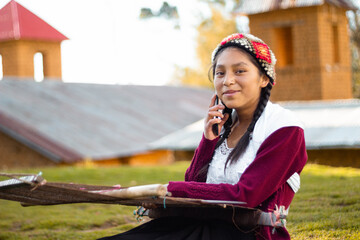 Foto de una feliz campesina caucásica hablando por teléfono inteligente y sosteniendo un tejido de manta artesanía peruana a mano en un atardecer en los Andes peruanos. Mujer usando teléfono móvil - obrazy, fototapety, plakaty
