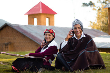 Un par de campesinos sentados muy alegres hablando por teléfono celular al aire libre, mujer y...