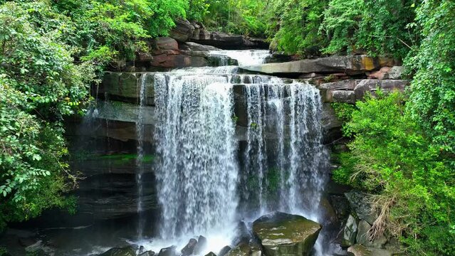 Mesmerizing tropical waterfall cascades from towering cliff, captured by a drone in epic aerial view. Thung Na Muang Waterfall, Pha Taem National Park, Ubon Ratchathani Province, Thailand. 4K.
