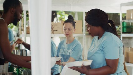 Young charity workers, serving fresh food to those in need, offering support and relief to homeless people and refugees. Poor and hungry individuals receiving free meals at outdoor food bank.