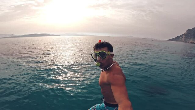 One young beautiful active man jumping off a boat enjoying vacations outdoor in the sea snorkeling looking for fished and coral. Male person traveling holding camera having fun in the blue ocean

