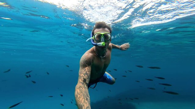 One young beautiful active man swimming and enjoying vacations outdoor in the sea snorkeling looking for fished and coral. Male person traveling holding camera having fun in the blue ocean
