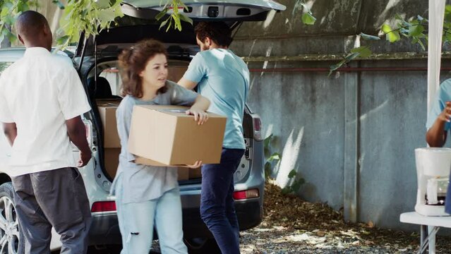 Less fortunate caucasian woman and african american man are seen accepting donation box from male volunteer at a food drive. Charity worker distributes essentials to the needy and homeless people.