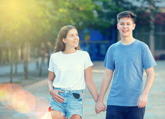 Two teenagers are walking hand in hand in summertime