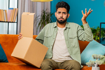 Angry dissatisfied shopper Indian man unpacking parcel feeling upset and confused with wrong...