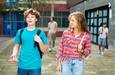 Teenager boy and girl going home after classes in school and having conversation.