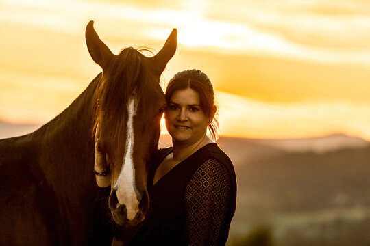 A young female equestrian and her arab berber horsein front of a romantic sunset landscape. Bond between a woman and her horse