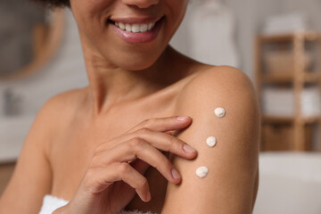 Young woman applying body cream onto arm in bathroom, closeup