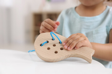 Motor skills development. Little girl playing with wooden lacing toy at table indoors, closeup