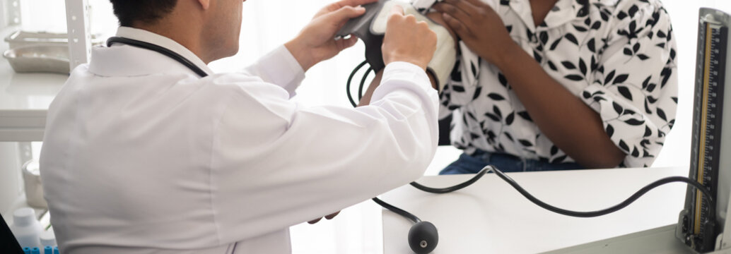 Hispanic doctor measuring African American patient's blood pressure. Person medical healthcare and wellbeing, the physician meet with patient at clinic concept.