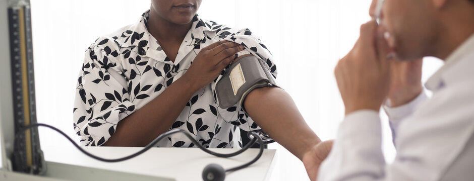 Hispanic doctor measuring African American patient's blood pressure. Person medical healthcare and wellbeing, the physician meet with patient at clinic concept.