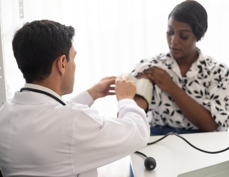 Hispanic doctor measuring African American patient's blood pressure. Person medical healthcare and wellbeing, the physician meet with patient at clinic concept.