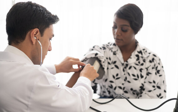 Hispanic doctor measuring African American patient's blood pressure. Person medical healthcare and wellbeing, the physician meet with patient at clinic concept.