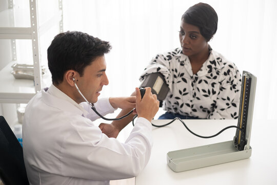 Hispanic doctor measuring African American patient's blood pressure. Person medical healthcare and wellbeing, the physician meet with patient at clinic concept.