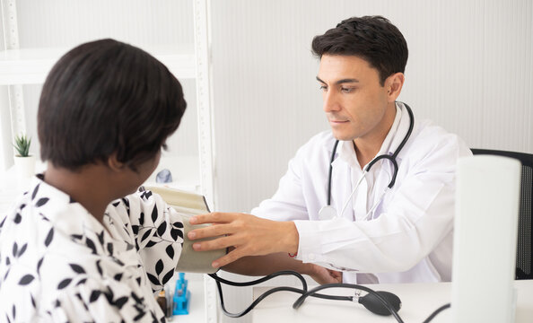 Hispanic doctor measuring African American patient's blood pressure. Person medical healthcare and wellbeing, the physician meet with patient at clinic concept.