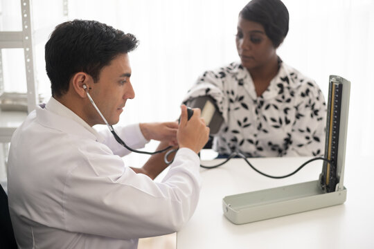 Hispanic doctor measuring African American patient's blood pressure. Person medical healthcare and wellbeing, the physician meet with patient at clinic concept.