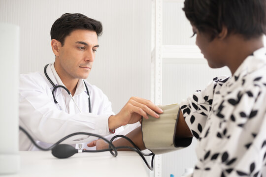 Hispanic doctor measuring African American patient's blood pressure. Person medical healthcare and wellbeing, the physician meet with patient at clinic concept.