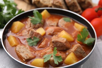 Delicious goulash in saucepan on table, closeup