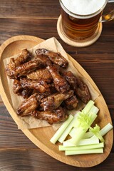 Delicious chicken wings served with cut celery stalks and beer on wooden table, flat lay