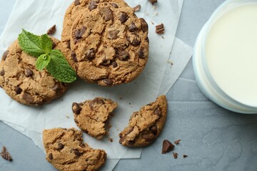Tasty chocolate chip cookies, glass of milk and mint leaves on light grey table, flat lay