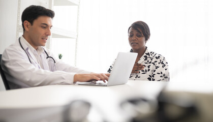 Hispanic physician check-up African American patient with stethoscope at the hospital. Healthcare medical diagnosis and examining on the laptop.