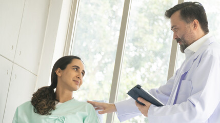 Caucasian male physician diagnosis for root cause finding working on tablet with Hispanic female patient. The medical healthcare exam and check-up with the doctor concept.