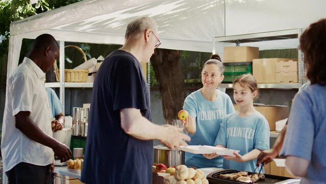 Poor, needy and homeless people receive meals and donations from friendly volunteers. Generous young girl handing out free food to underprivileged individuals at a non-profit food drive.