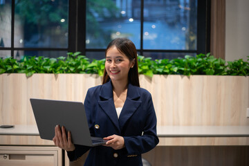 Happy young Asian saleswoman holding laptop. Smiling business woman agent broker, Standing in the modern office. Successful posture portrait.