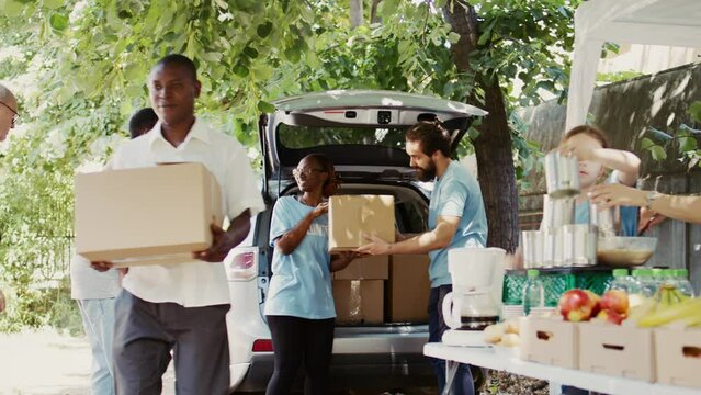 An outdoor non-profit food drive program to aid the poor needy and homeless people. Young multiethnic volunteers giving donation boxes from the car to the less privileged. Handheld shot.