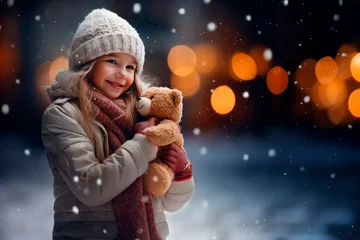 Foto auf Acrylglas A young girl with a teddy bear in her hands smiling on a snowing happy holiday  © Ágerda