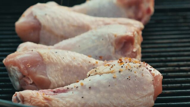 Raw chicken drumsticks on a bbq grill being seasoned 