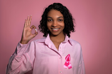Breast cancer awareness concept.Smiling,cheerful girl with pink ribbon showing ok sign