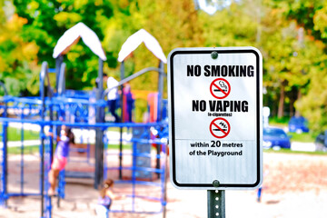 No Smoking and No Vaping sign with blurred children playing at outdoor playground at park.